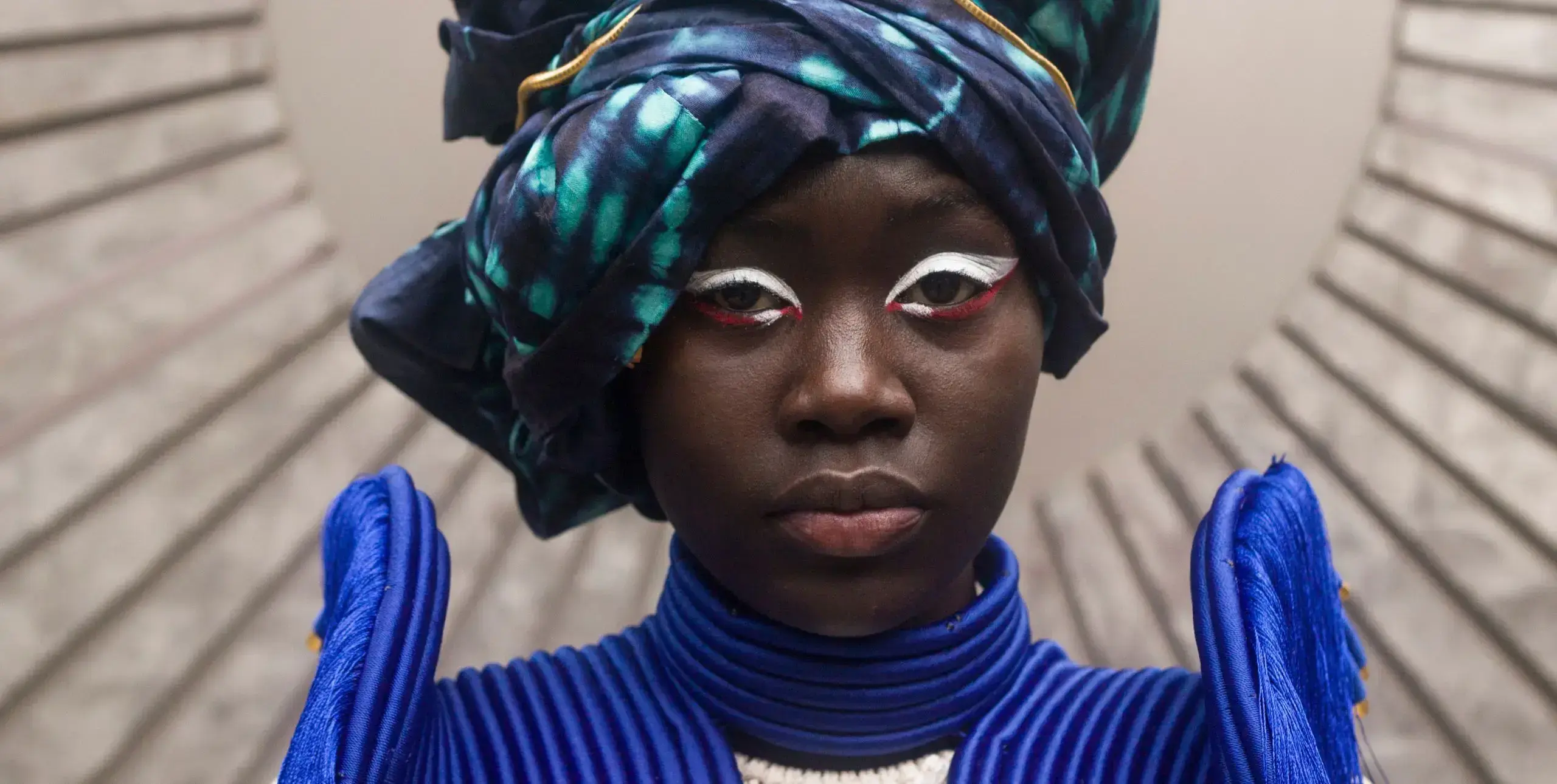 A woman models a tie-die turban and jacket with high epaulettes
