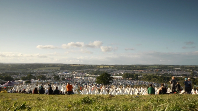 A view over Glastonbury festival during daytime with people stood looking forwards.