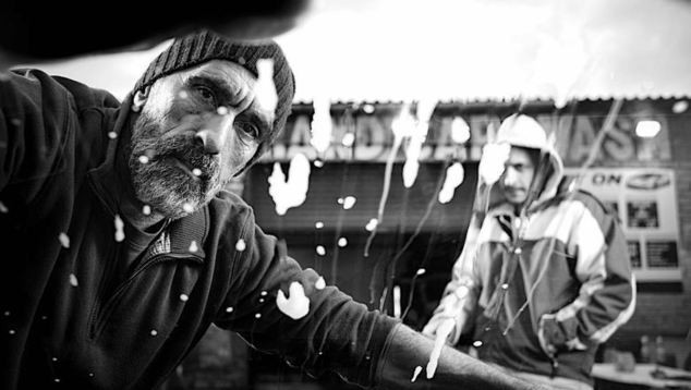 The Ceremony, directed by Jack King is one of 14,000 entries in our UK Film database. A still from a black and white film showing an older man wearing a beanie hat looking into the camera frame through a window which he is washing. Behind him stands a younger man wearing a hooded jacket. Streaks of soapy water are smudged across the frame.