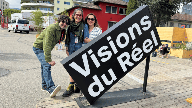 Elahe Esmaili and members of the A Move team attend Visions du Réel in Switzerland. A man and two women stand on an urban street behind a large black and white sign that reads 'Visions du Réel'.