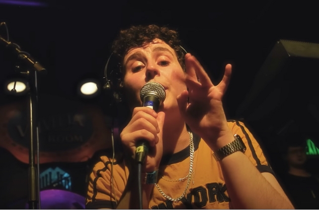 Singer close up, with headphones on, singing into held microphone.