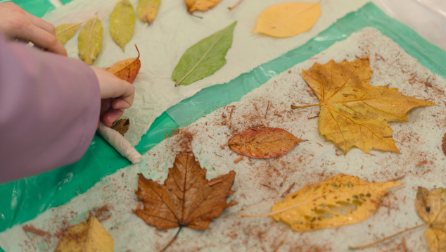 A close up of someone attaching autumnal leaves to scraps of fabric.