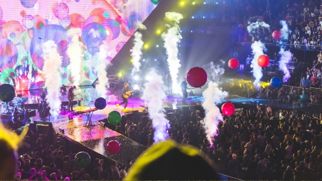 Live music event with guitarist on stage, balloons off stage and a crowd standing and seated.