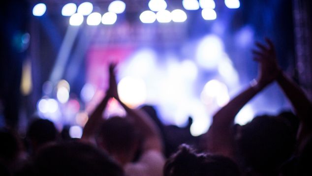 Audience members facing a concert stage clap their hands over their heads.