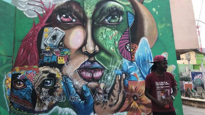 A man stands in front of a mural of a face in Colombia