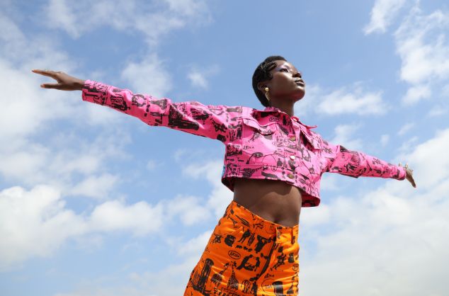 A black woman holds out her arms against a blue sky