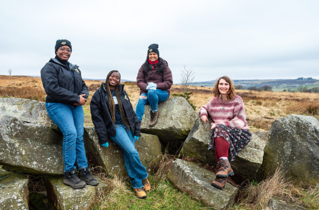 Four people aside, at the top of a hill, sitting on rocks, smiling and looking towards us.