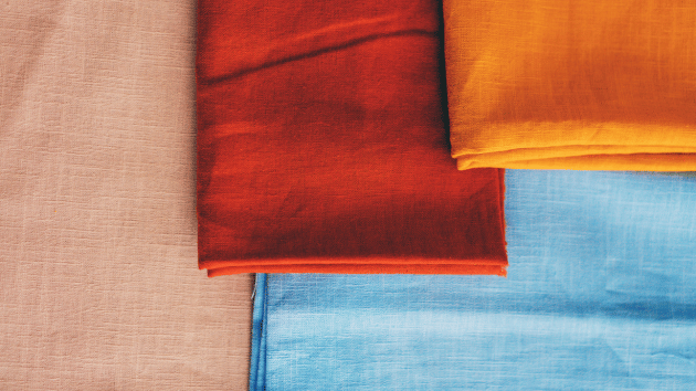 Folded squares of linen fabric overlapping each other. The fabrics are pale pink, terracotta orange, bright yellow and light blue. (c) Getty