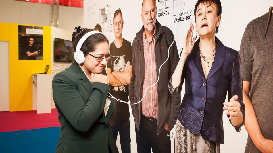 A lady smiling, wearing headphones connected to an exhibition.
