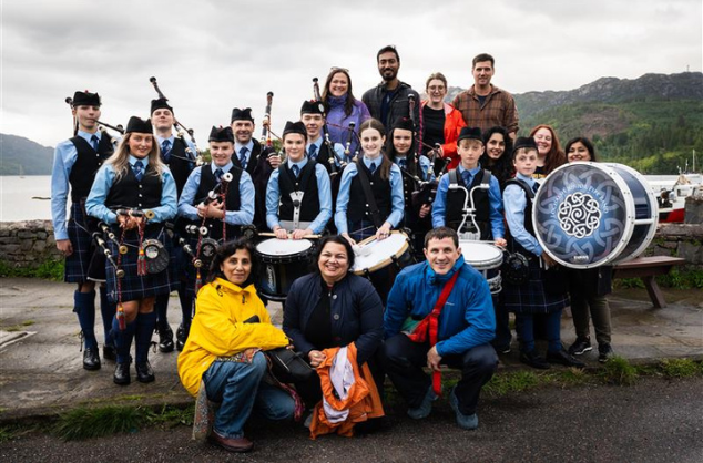 A large group of musicians sit together, holding instruments and dressed in traditional Scottish dress. Mehfil Ceilidh delegates from Pakistan meeting with the Lochalsh Junior Pipe Band and Atlas Arts © Magnus Graham