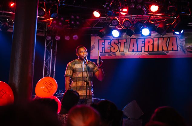 A man speaks to an audience on stage with a Fest Afrika banner behind him