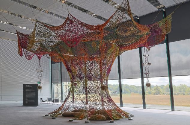 A multi coloured macrame effect tree artwork fills a gallery space from floor to ceiling