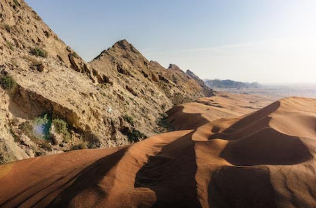 A landscape of rocky mountains and desert sand dunes