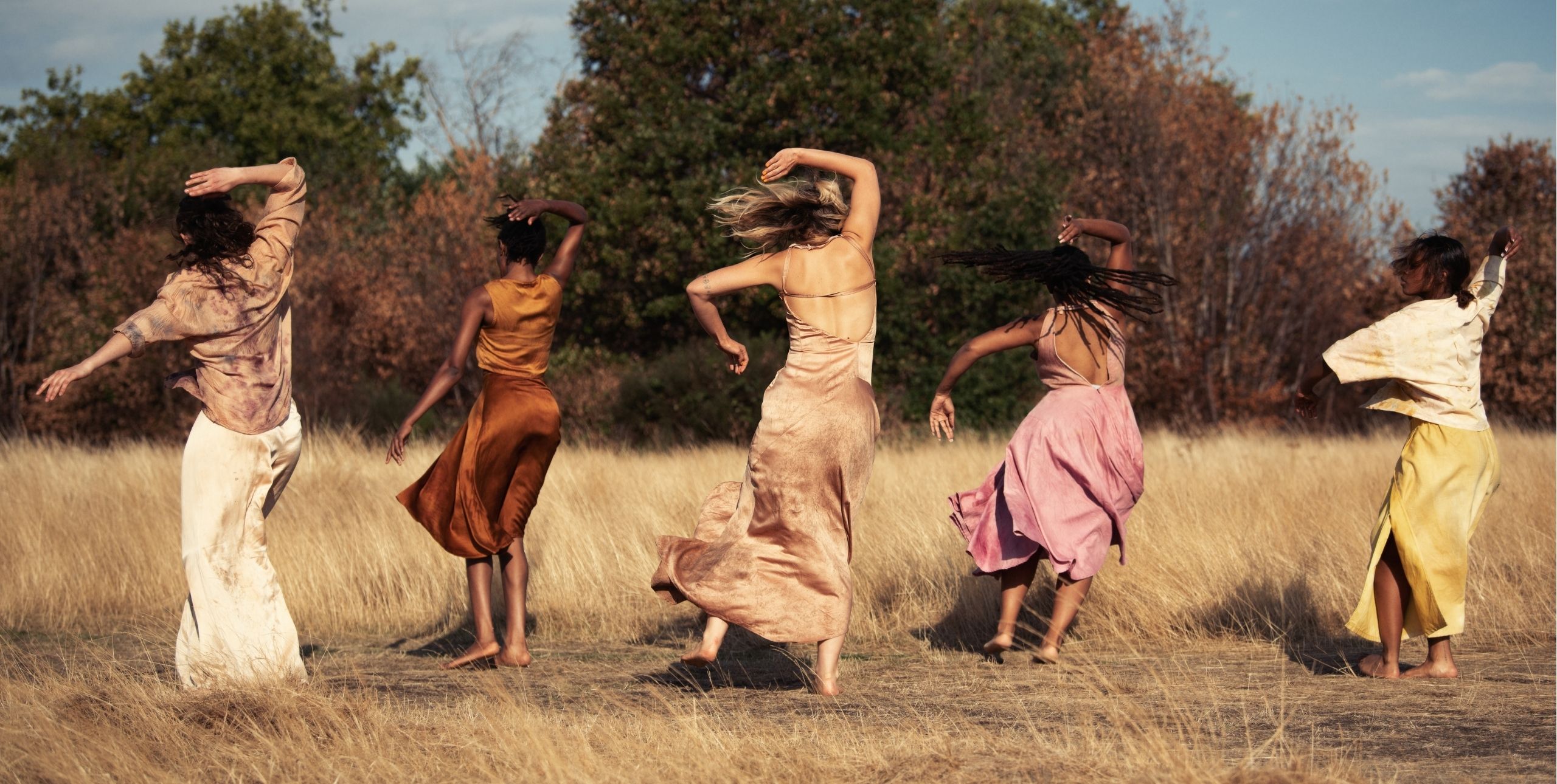 Five women in flowing dresses dance in a field