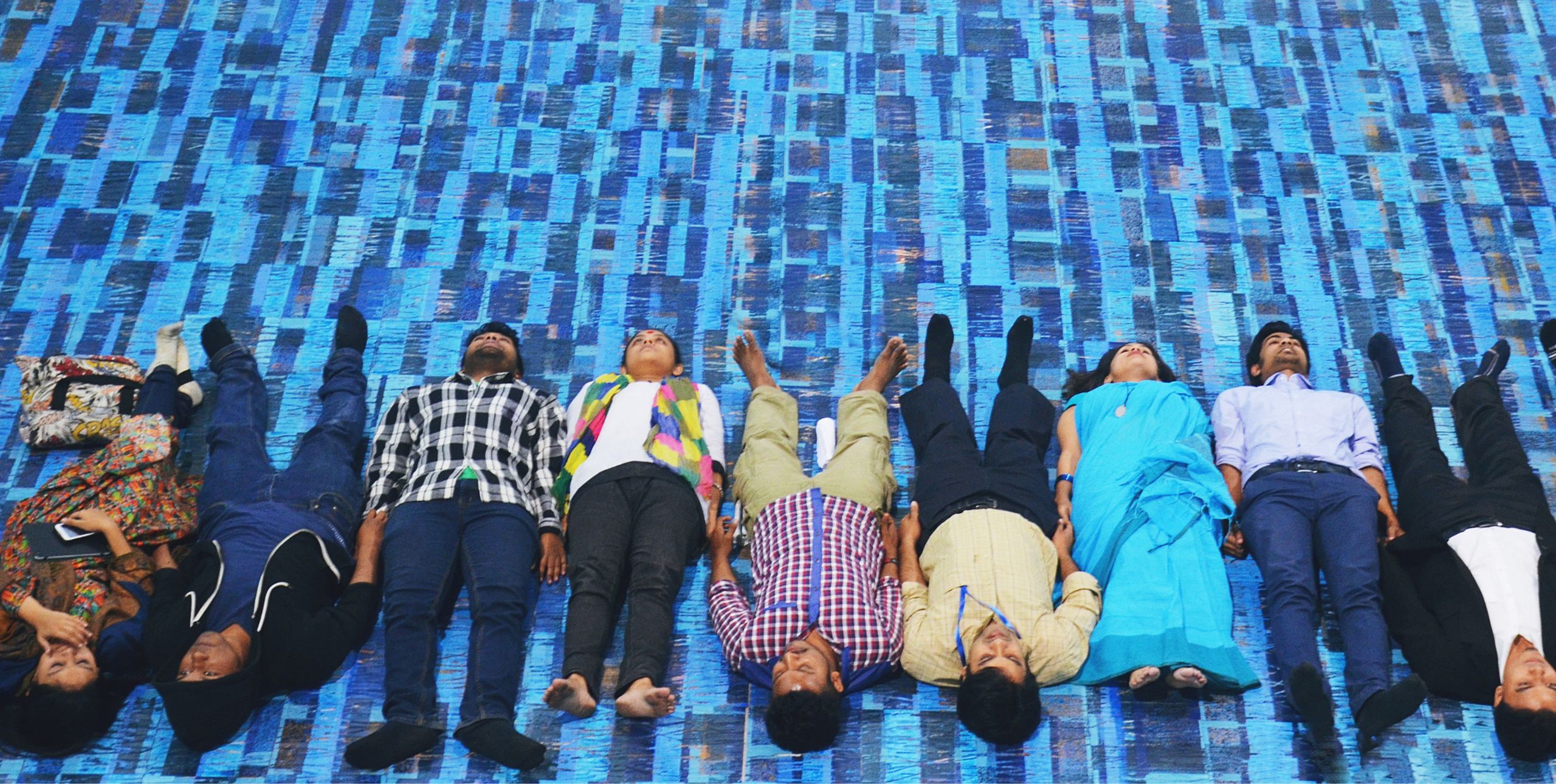 Young people lying on their backs in a row all next to each other, looking upwards from a bright background.