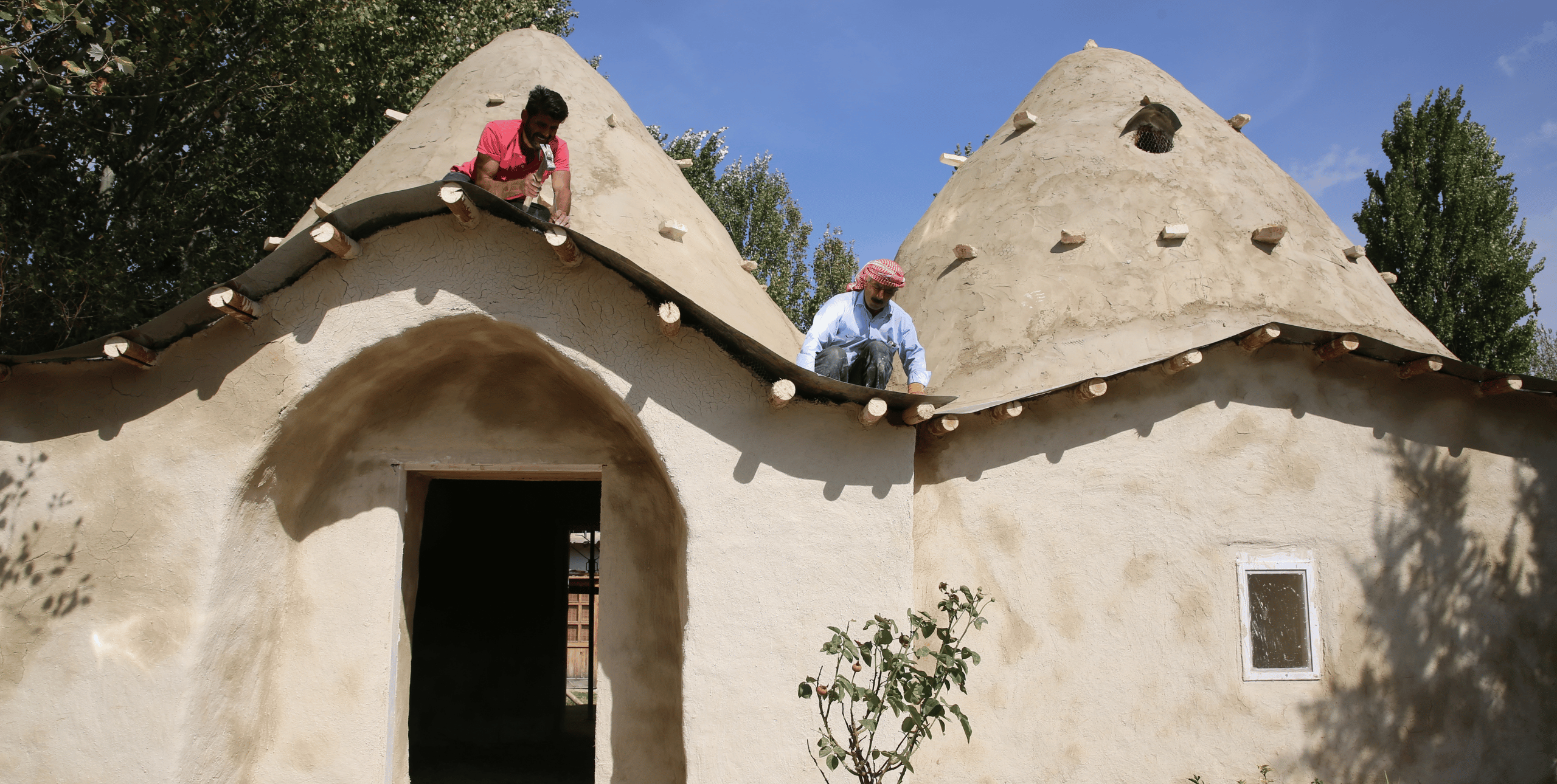 Syrian Dome Houses project. Two men work on the rooftop of a domed building in the sunshine.