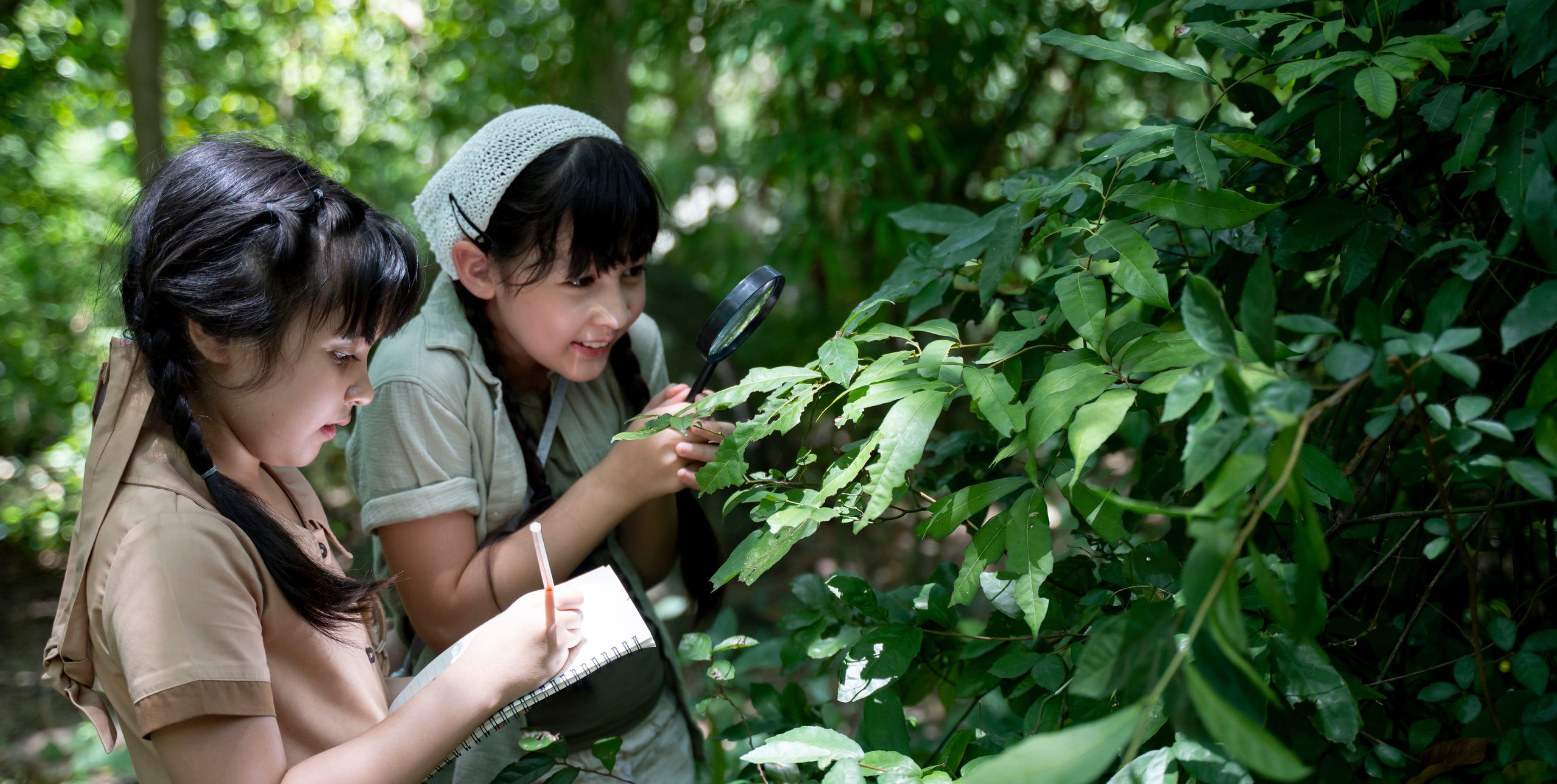 Two children study a plant and write in a book