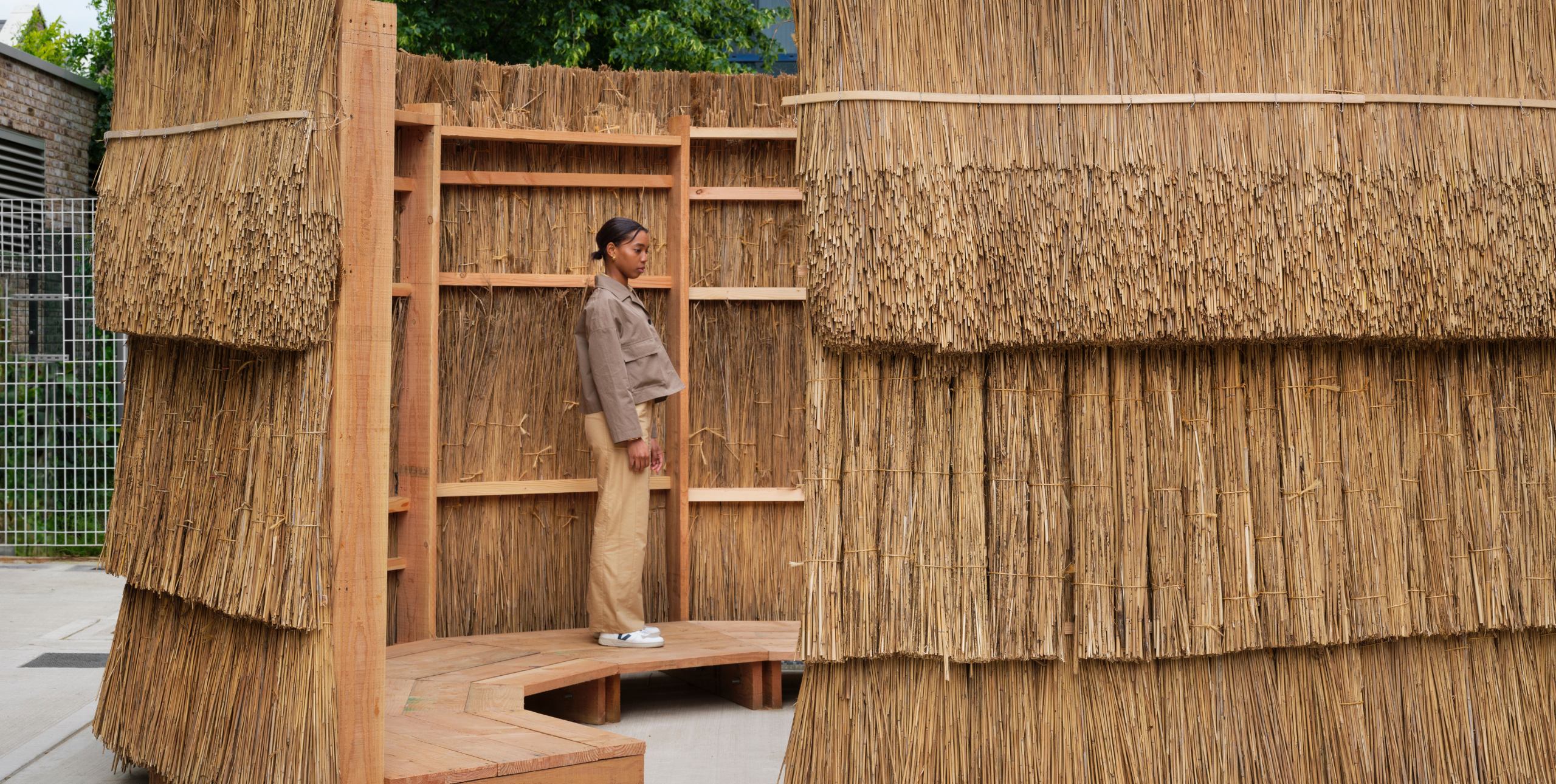 A girl stands in a simple wooden structure that is thatched with straw as part of the AHFA festival.