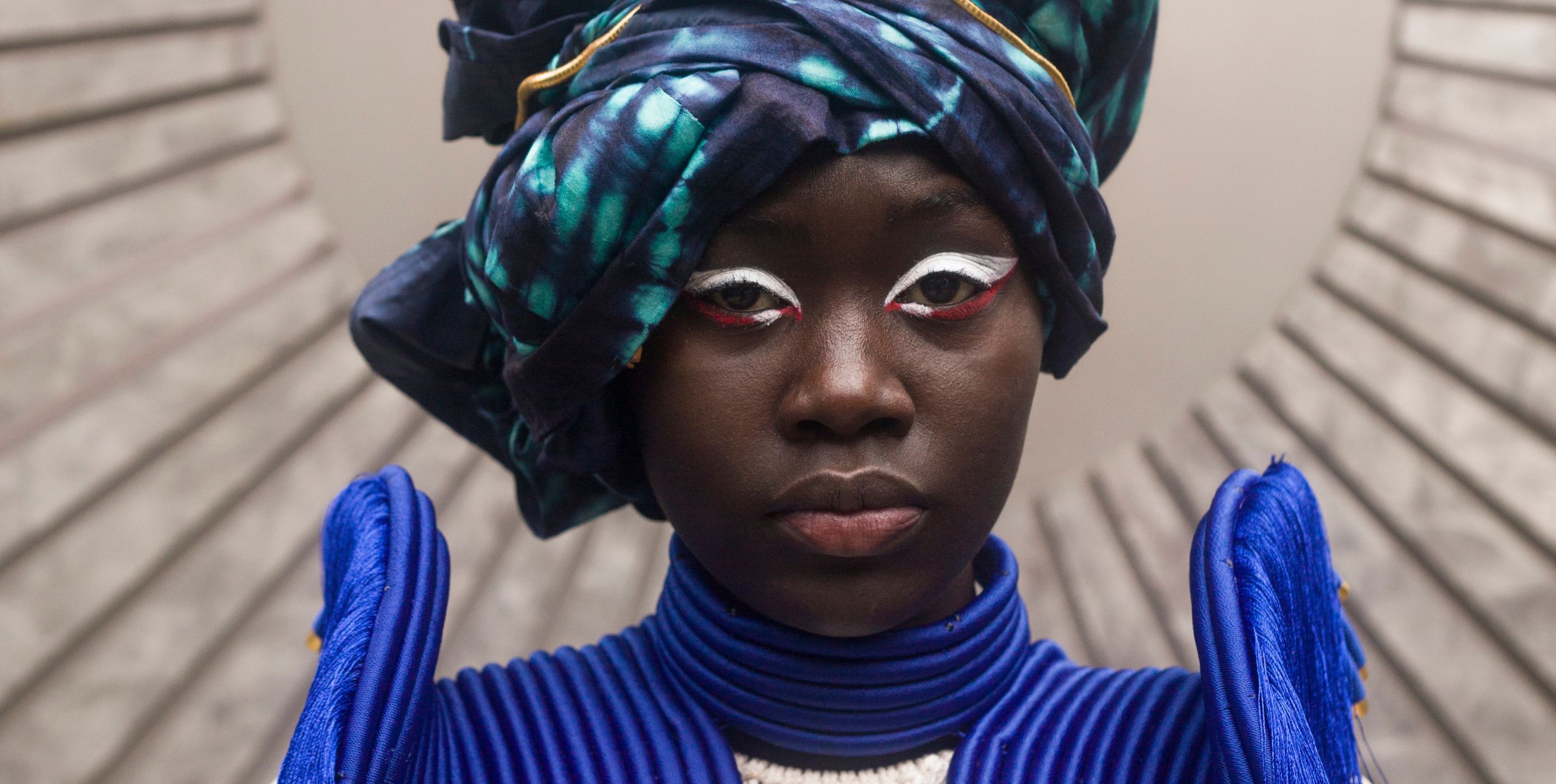 A woman models a tie-die turban and jacket with high epaulettes