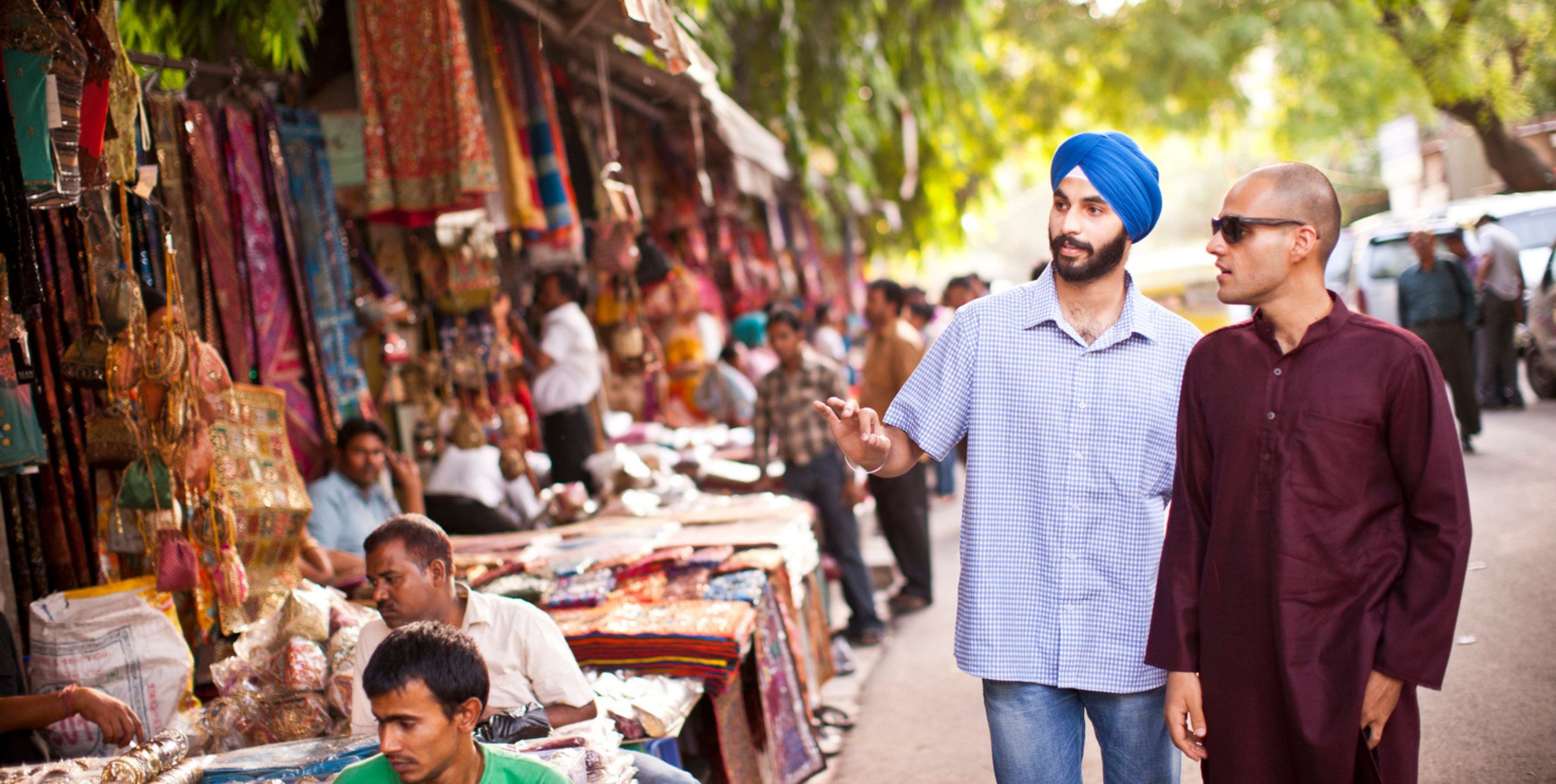 Two men pass a row of stalls selling handicrafts in an Indian city