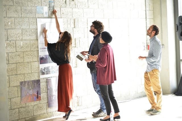 Four people pin papers to a brick wall.