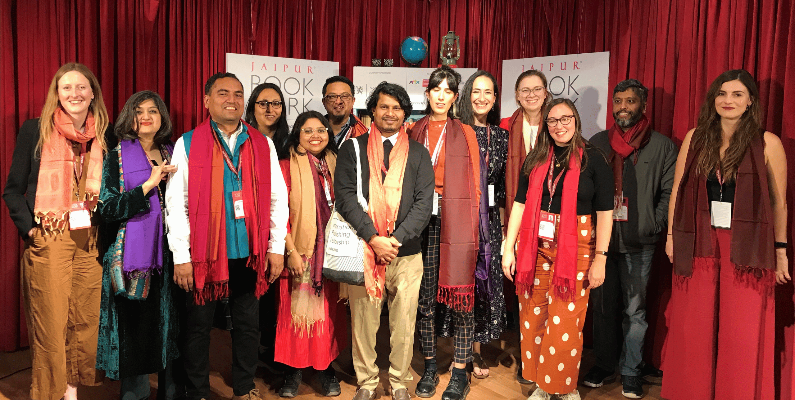 A group of smiling delegates stand on a stage in a line, with red curtains hanging behind them.