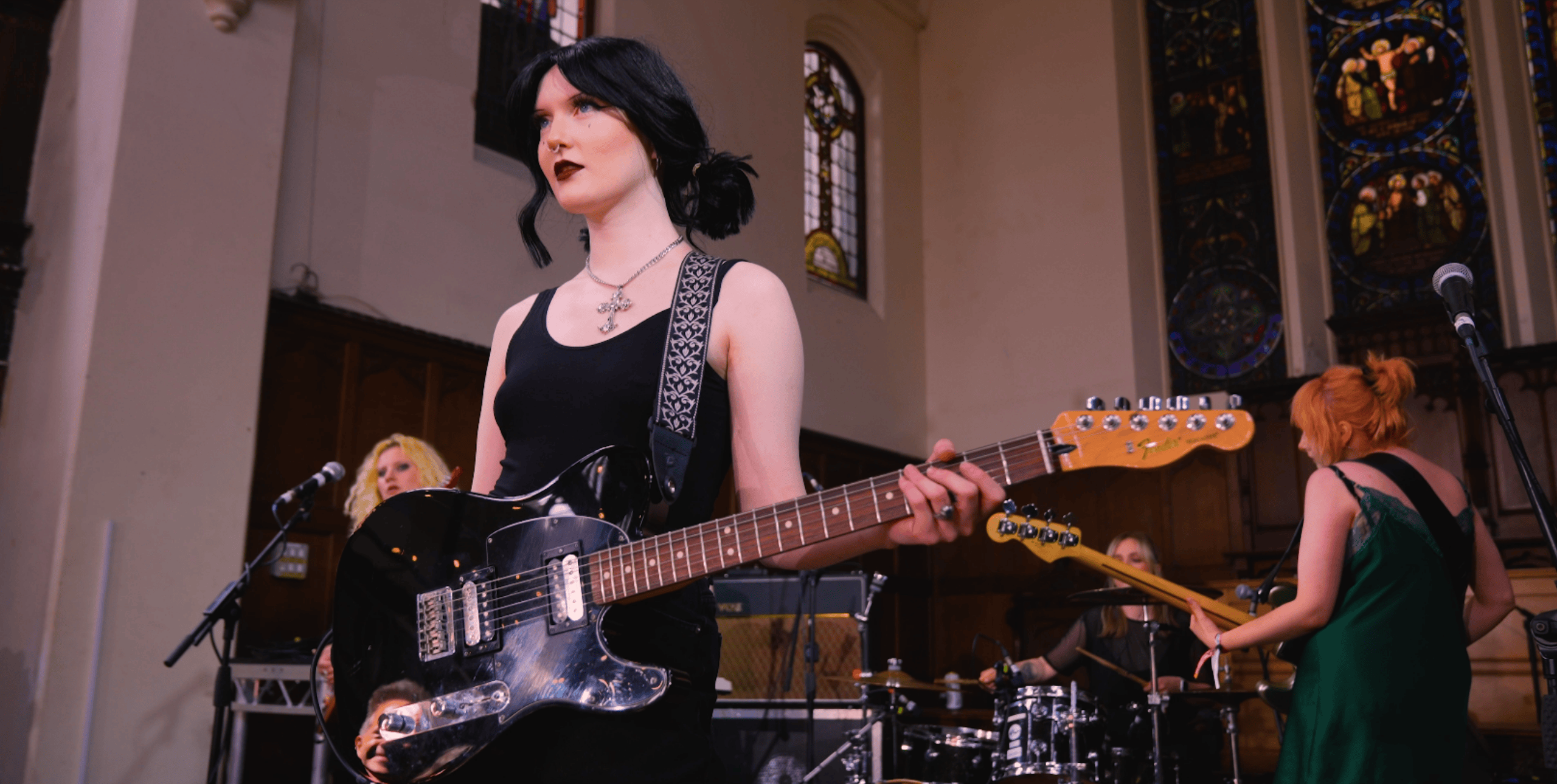 Venus Grrrls performing at The Great Escape 2024. A woman with dark hair and dark lipstick stands on a stage holding a black electric guitar.