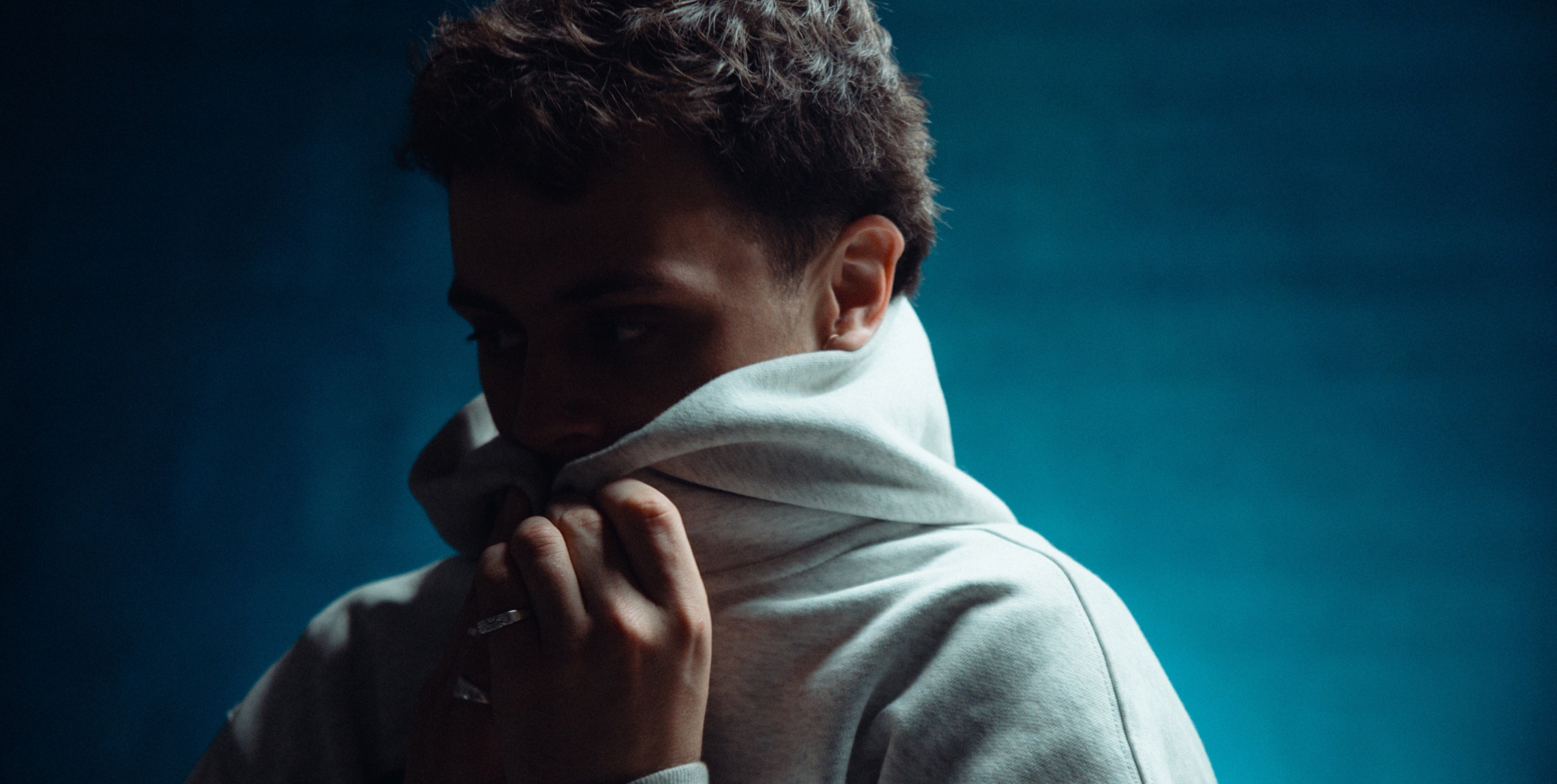 Man with short hair pulling a hoodie up around his chin.
