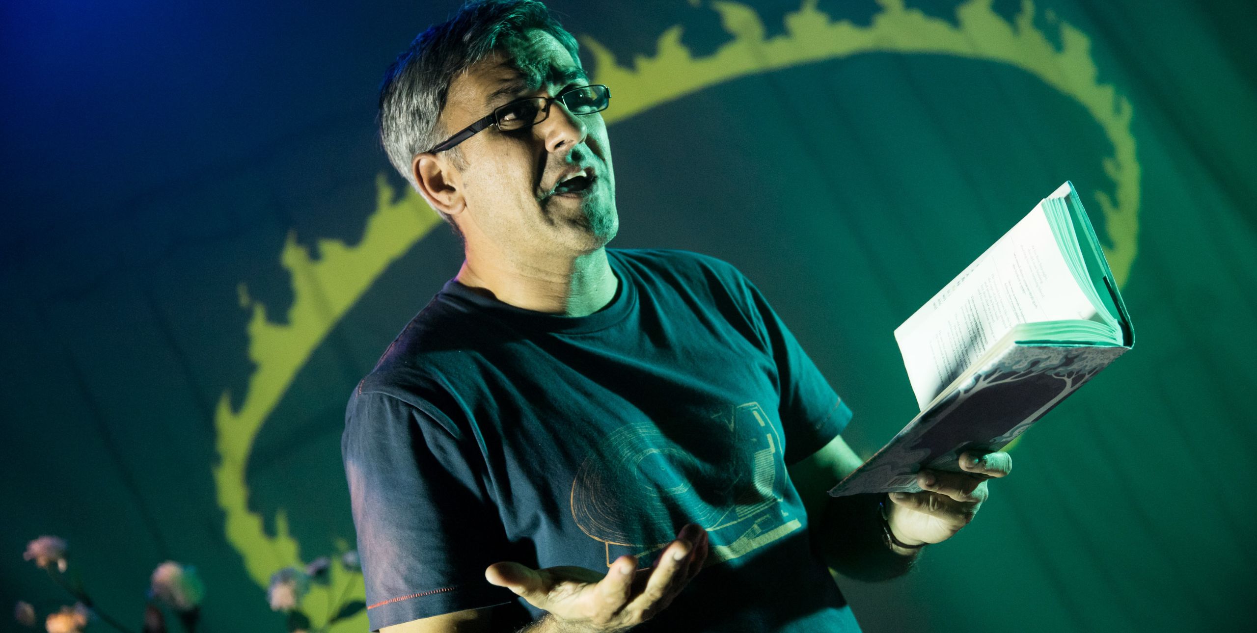 British Poet Daljit Nagra stands on stage and animatedly reads from an open book