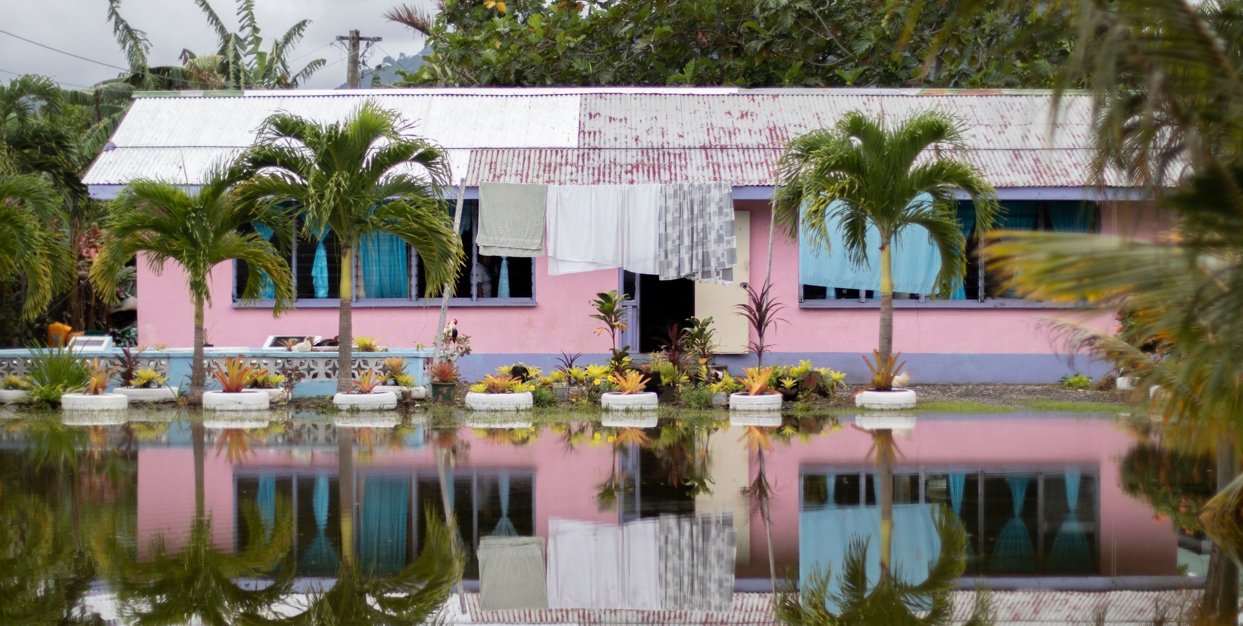 A pink bungalow is reflected in the huge puddle of water in front of it
