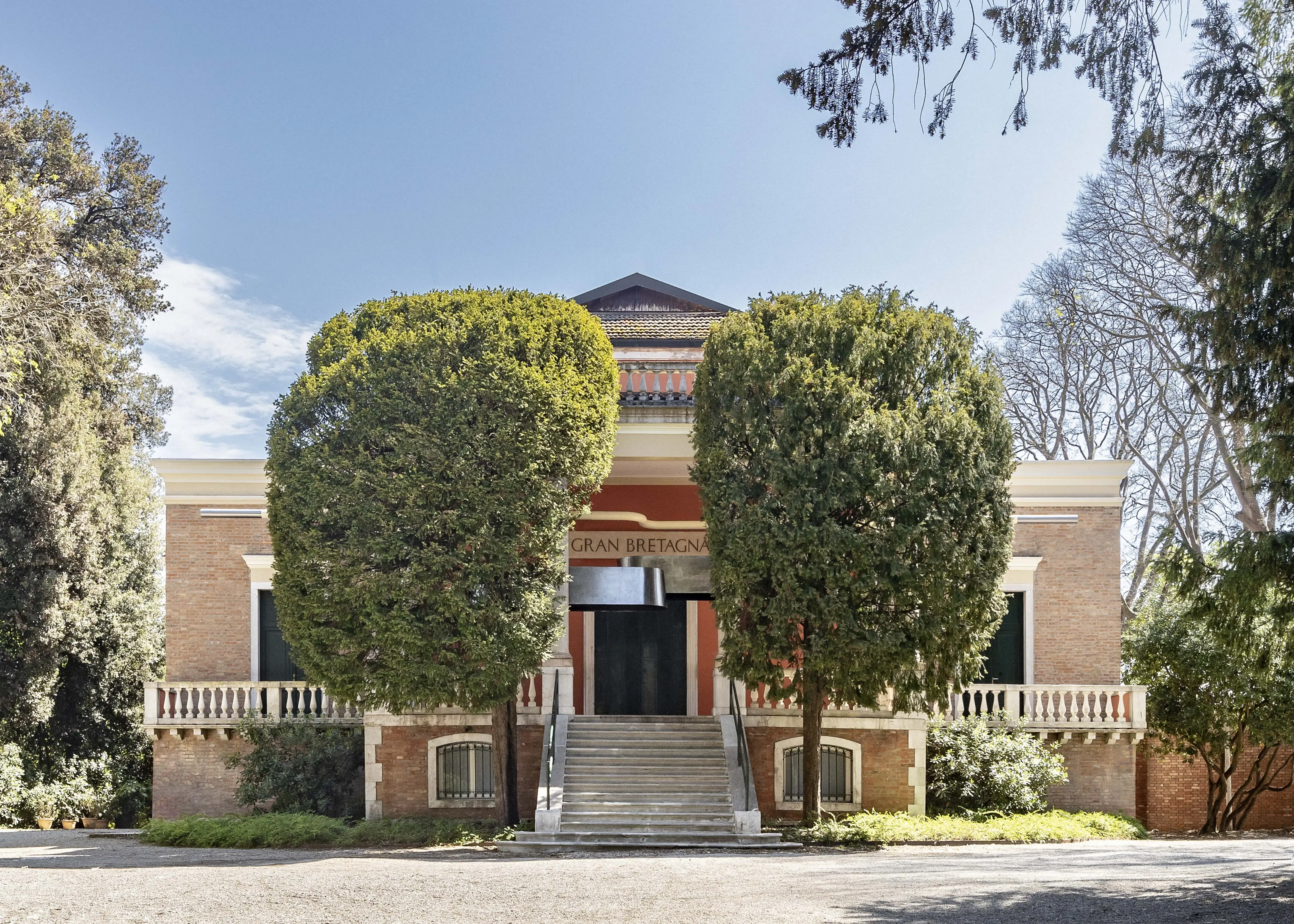 British Pavilion building portico, with two trees obscuring its frontage and a suspended silver sculptural from visible at the top of the steps.