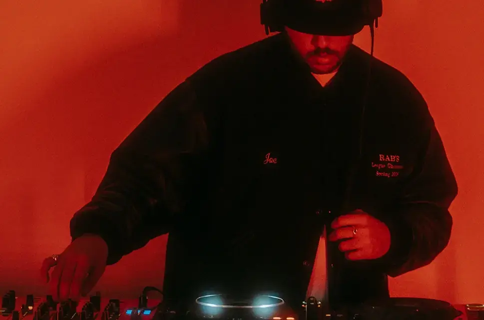 Close up of a DJ behind a mixing deck, wearing headphones, looking down, fingers on the controls.