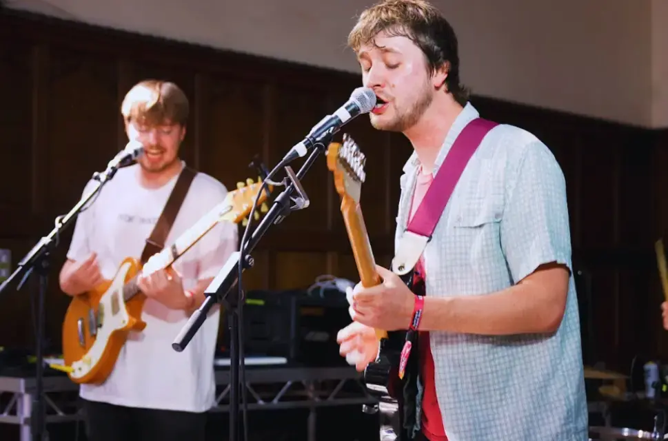 Two men playing electric guitars, singing into microphones.