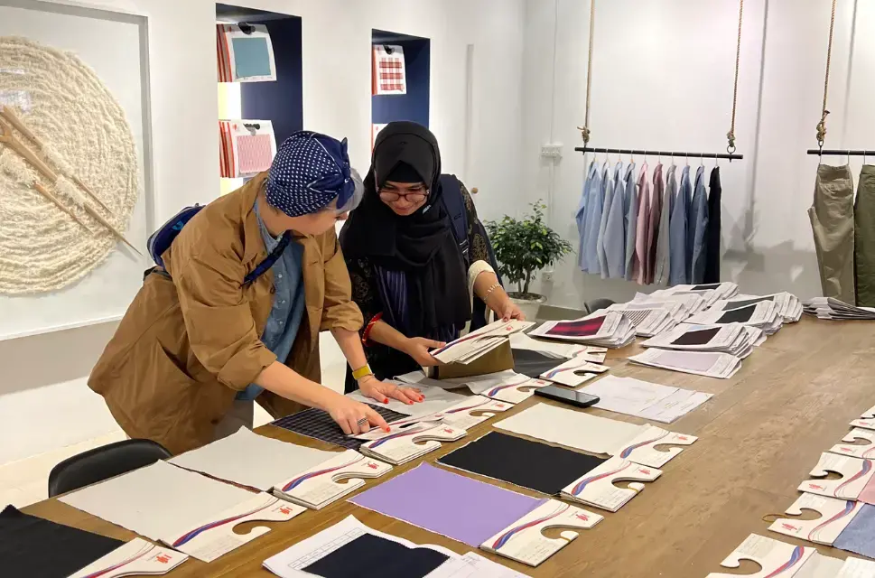 Two women work at a table together laying out fabric cuttings.