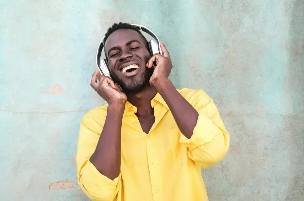 Man smiling, eyes closed, wearing and holding his hands around his headphones. 