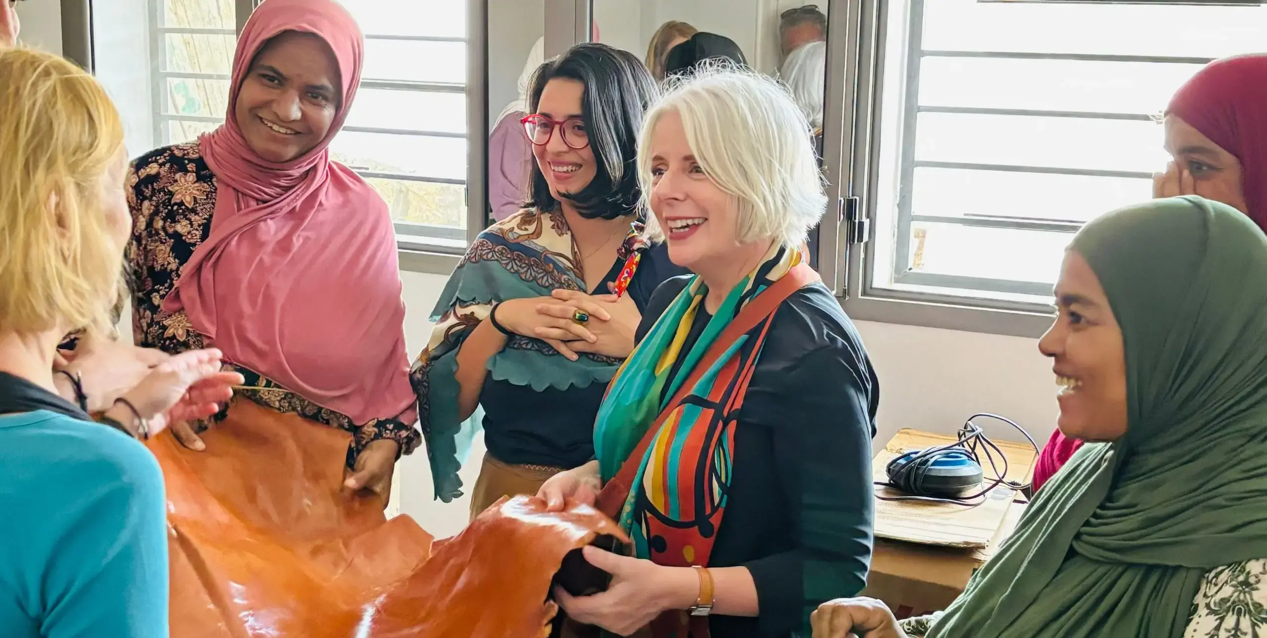 A group of women laugh and interact around a piece of leather