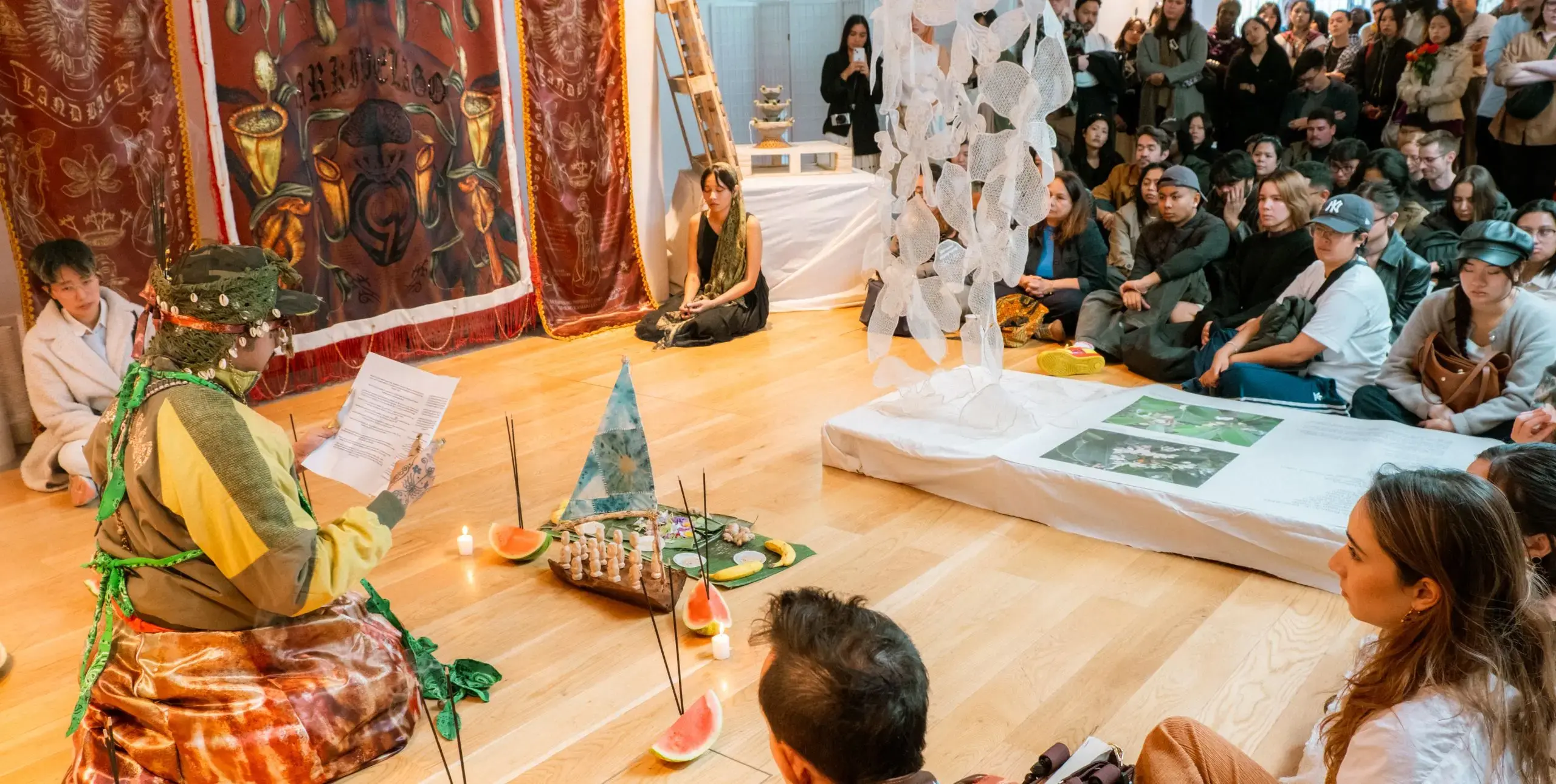 A seated person in traditional dress reads to an audience