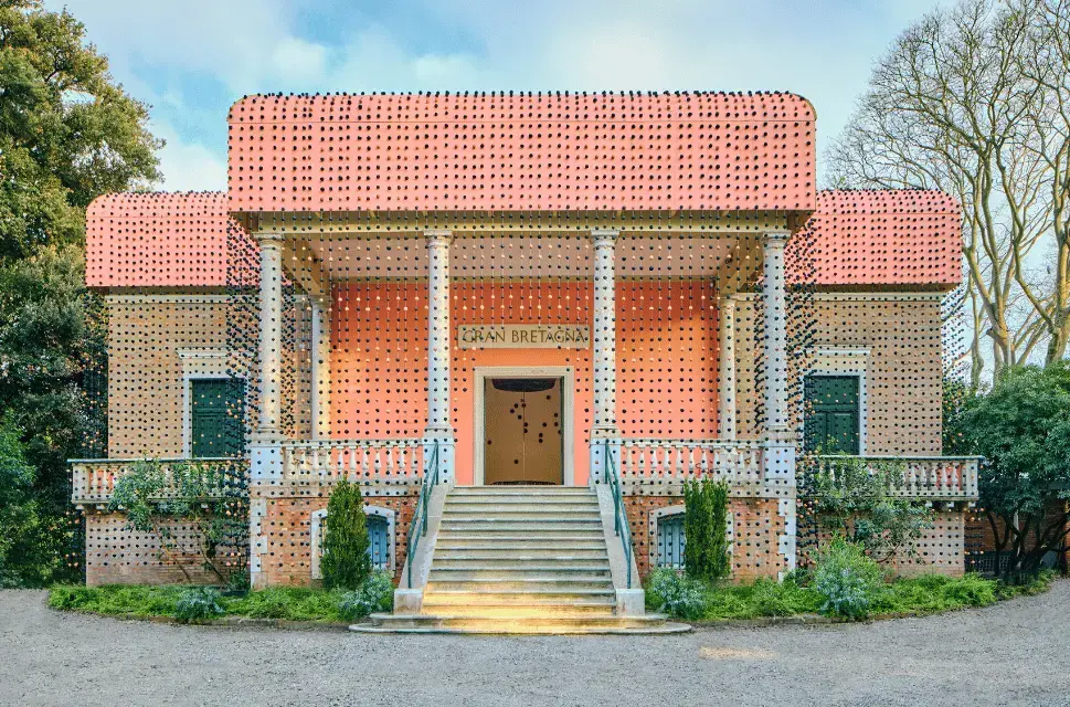 Portico of the British Pavilion at the Venice Architecture Biennale 2025. The facade of the Pavilion has been covered in black and orange beads made by Massai women