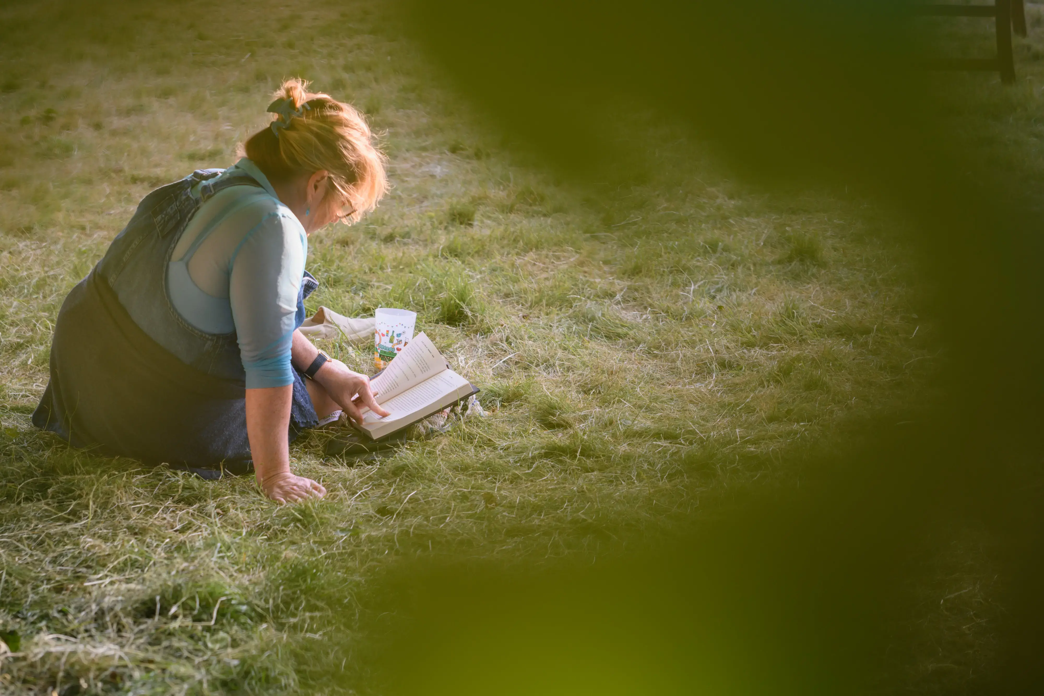 A woman at hay festival reads a book sat on the grass.