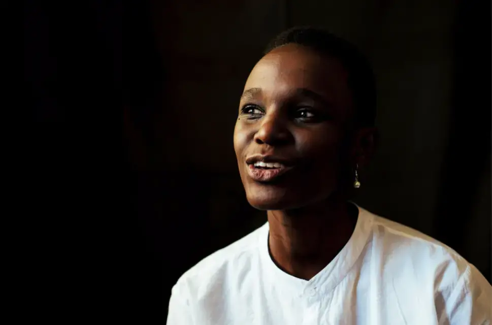 Lady with short hair, wearing white shirt, smiling, against black background.