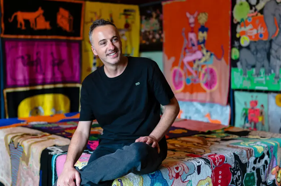 Man smiling, sat on and in front of, designs.