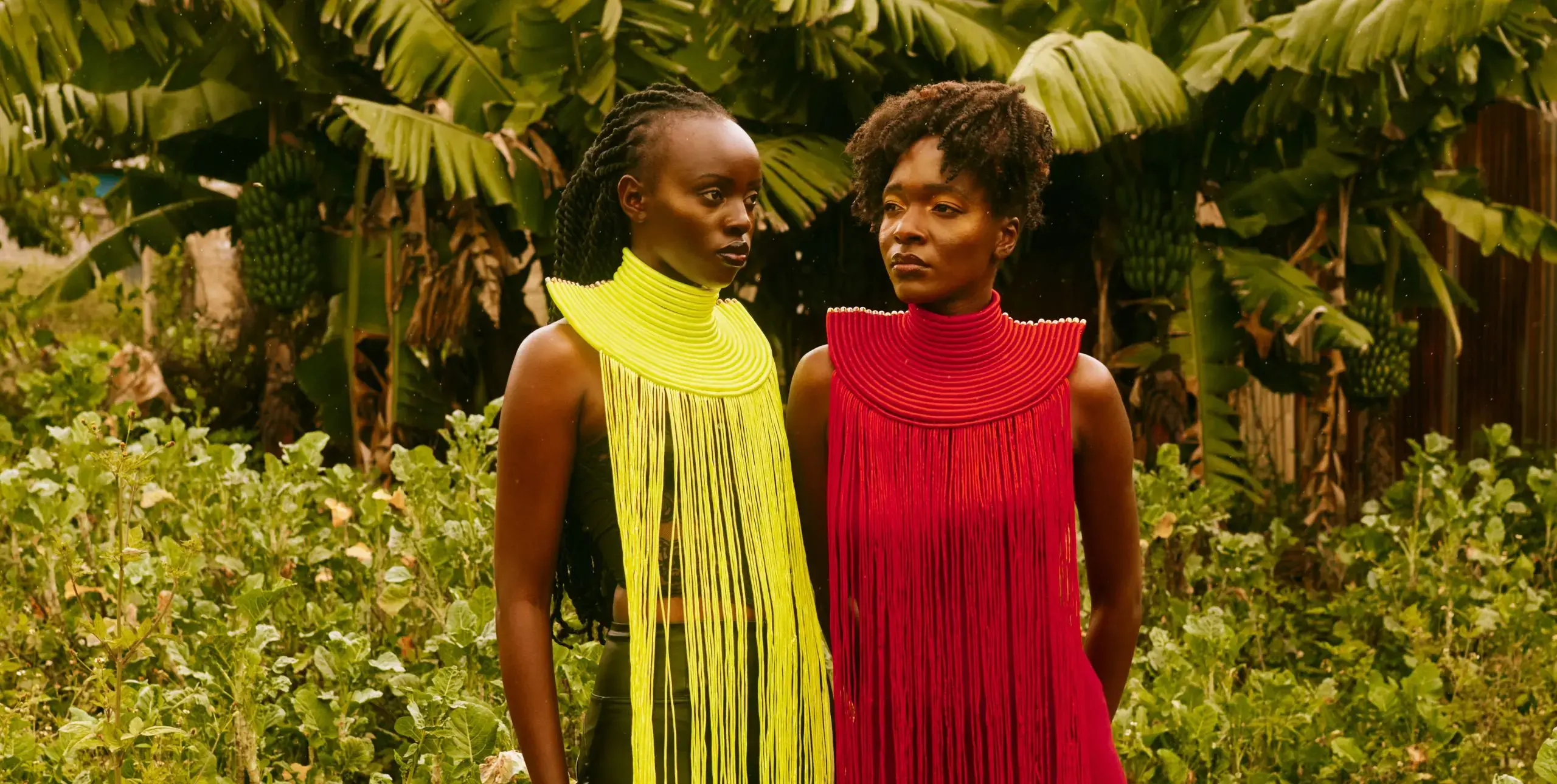 Two women in brightly coloured fringed collars against a tropical forest