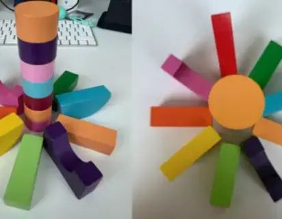 Colourful ooden building blocks are stacked together to make a flower stem and petals infront of a computer