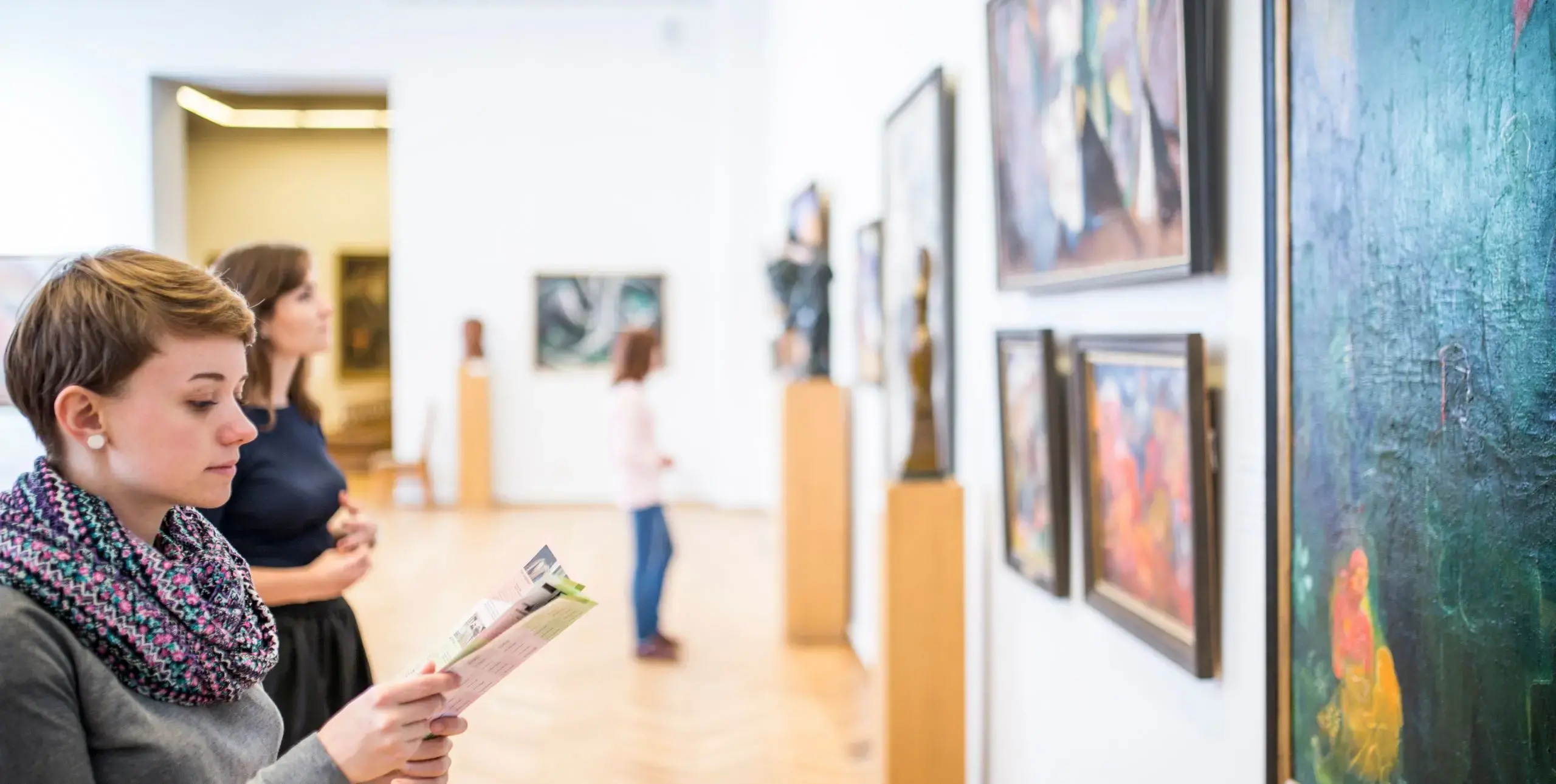 Two women look at large oil paintings in a large, bright art gallery in Kyiv, Ukraine.