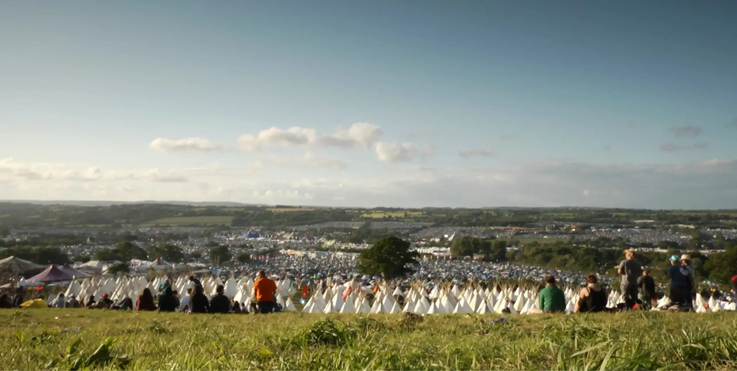 A view of the landscape over Glastonbury during the festival with people stood looking forwards.