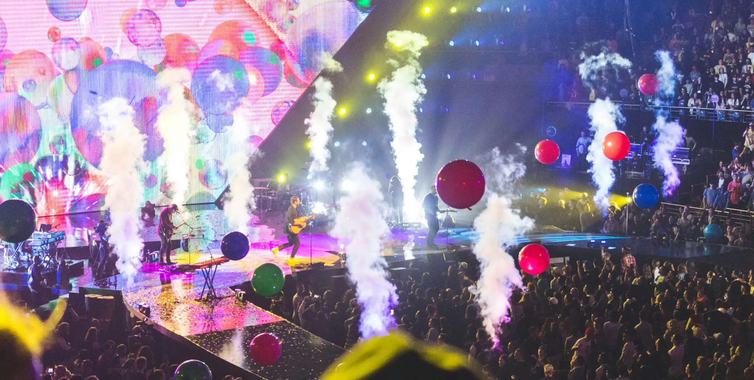 Live music event with guitarist on stage, balloons off stage and a crowd standing and seated.