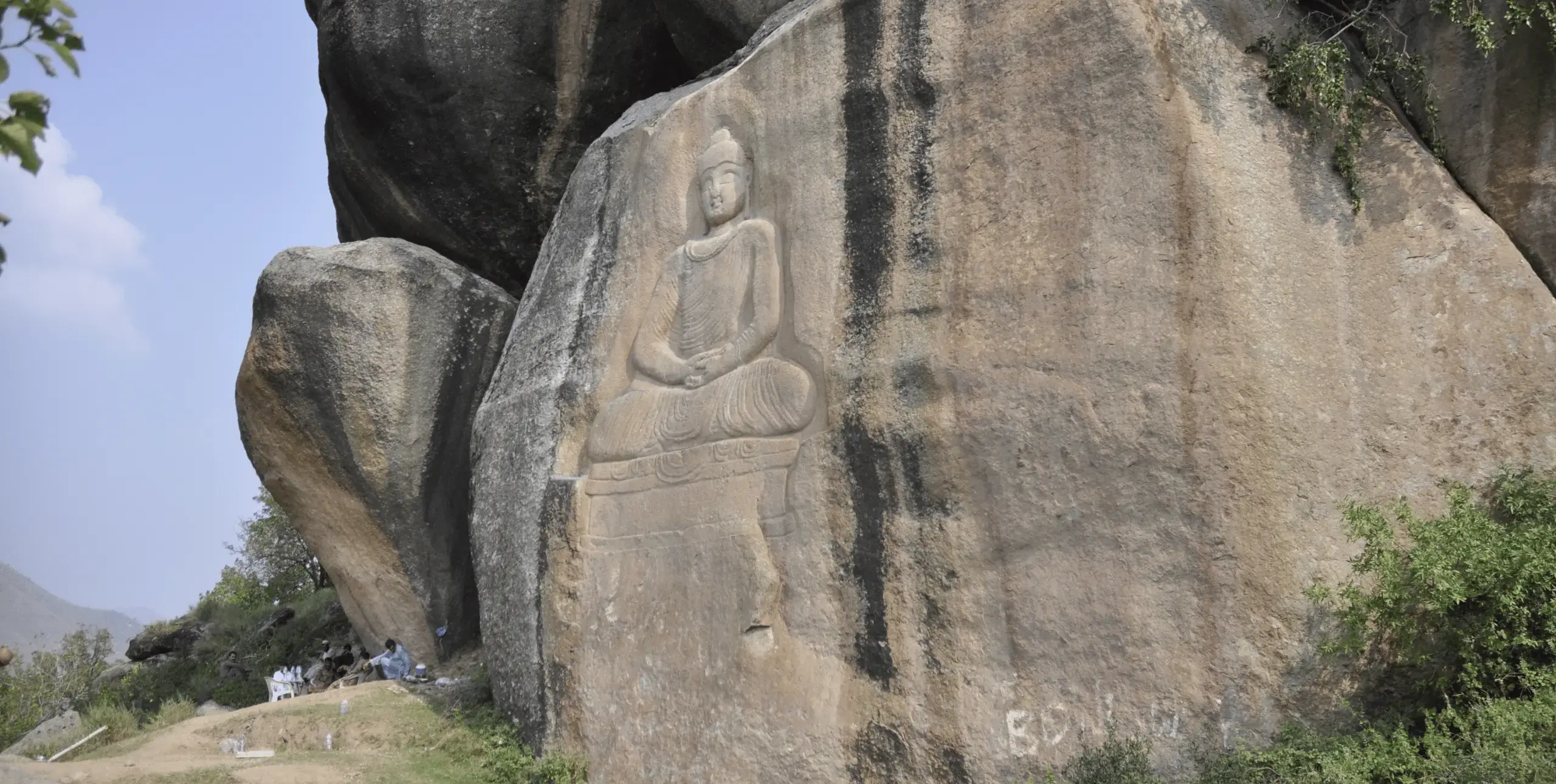 An image of The Buddha carved into the side of a large boulder or mountainside