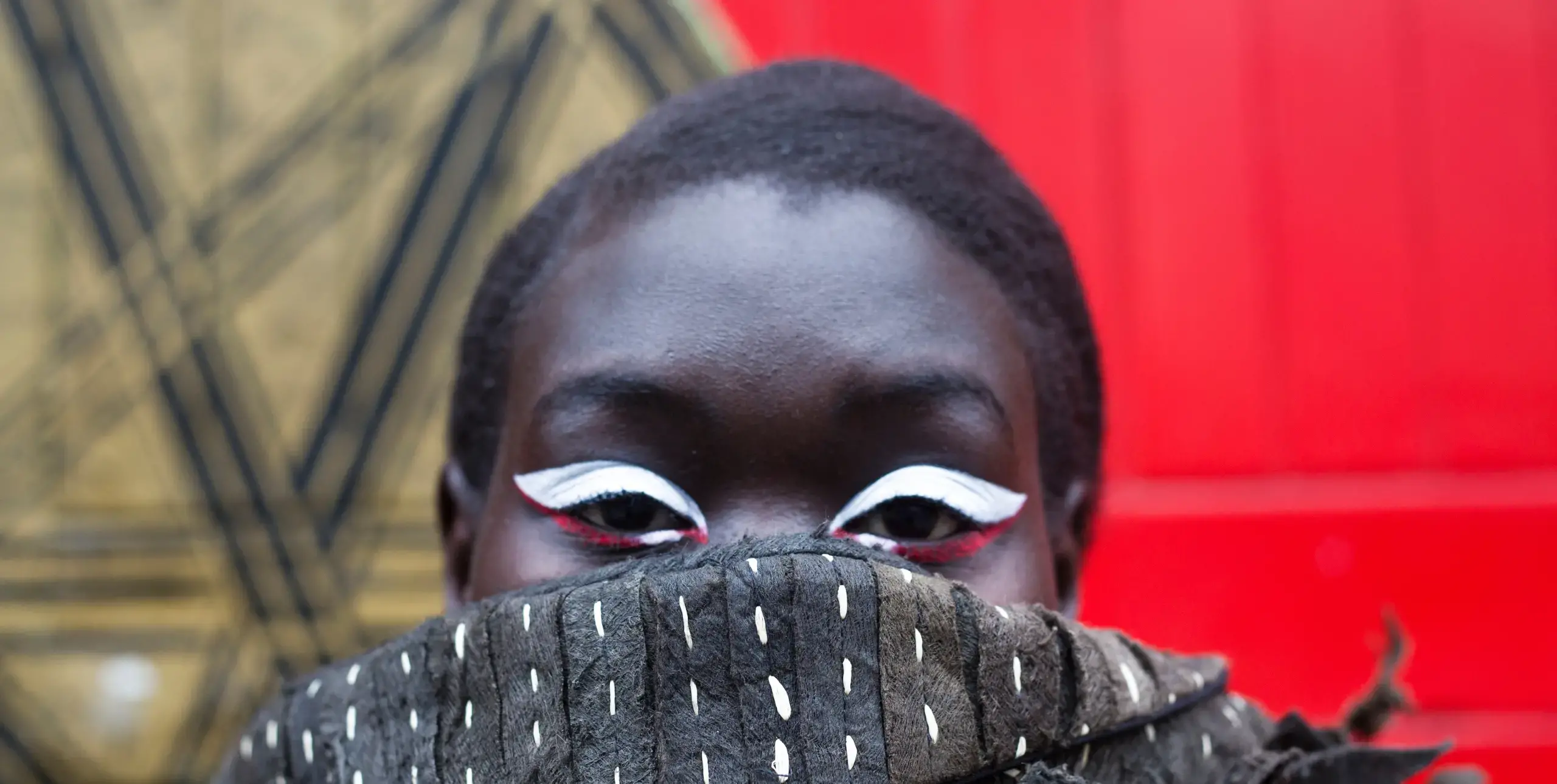 Striking eyes with white eyeliner stare over the top of a woolly scarf for a fashion photo shoot