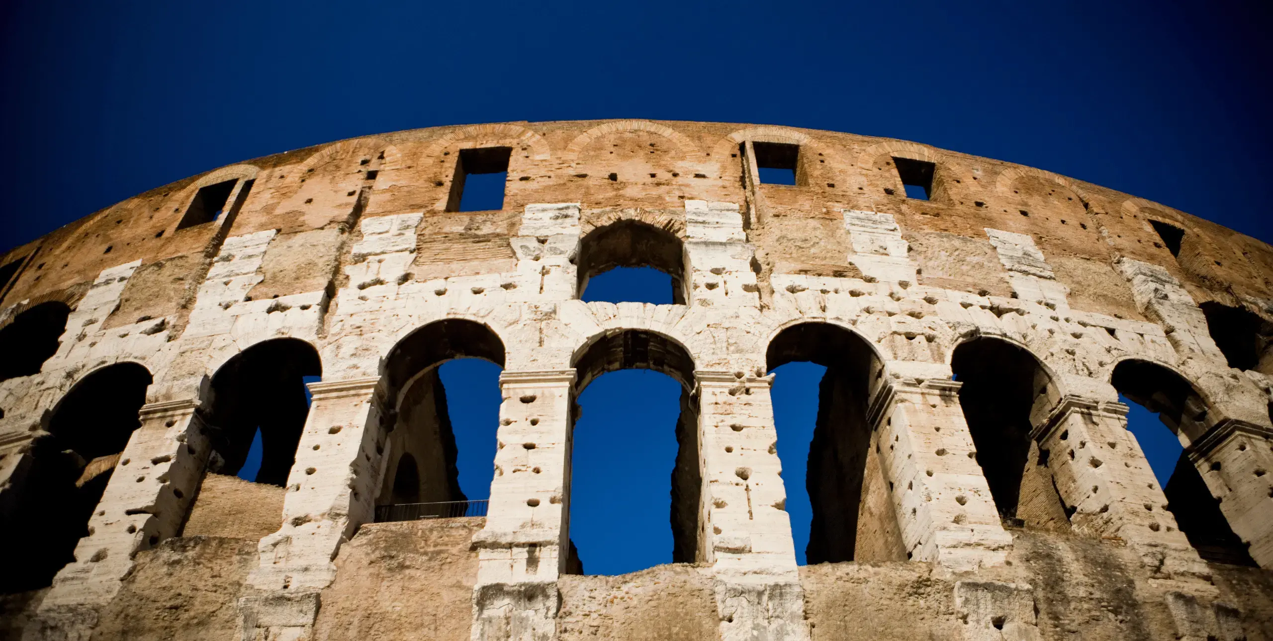 The Colosseum in Rome, photographed from beneath, with bright blue sky showing above and in betweem the columns.