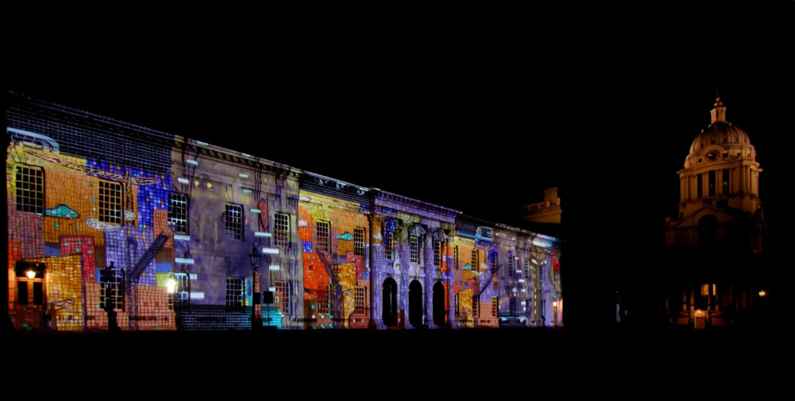 A row of historic looking brick buildings are lit up with colourful projections at night